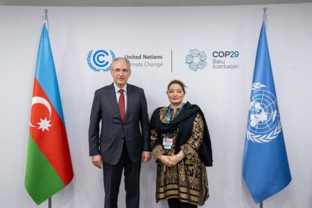 Coordinator to the Prime Minister on Climate Change, Romina Khurshid Alam, standing with an international delegate at COP29 in Baku, Azerbaijan, with UN and national flags in the background.